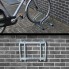 Cykelstativ til 2 cykler – galvaniseret stål med buede støttearme og 4 monteringshuller, set forfra mod en murstensvæg.