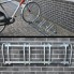 Cykelstativ til 4 cykler – galvaniseret stål i grå og sølv med 4 monteringshuller, set forfra mod en murstensvæg.